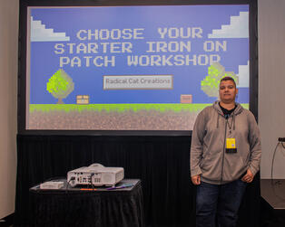 The artist stands in front of a projection that says “Choose Your Starter Iron On Patch Workshop”