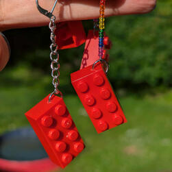 Lego brick earrings. One has a short chain and the other is on a pin with a stack of rainbow beads.